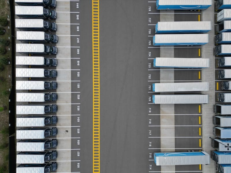 Top-down beeld van vrachtwagens in een logistiek parkeerterrein als illustratie van vlootschaal, laadvensters en depotlogica voor elektrische vrachtwagens